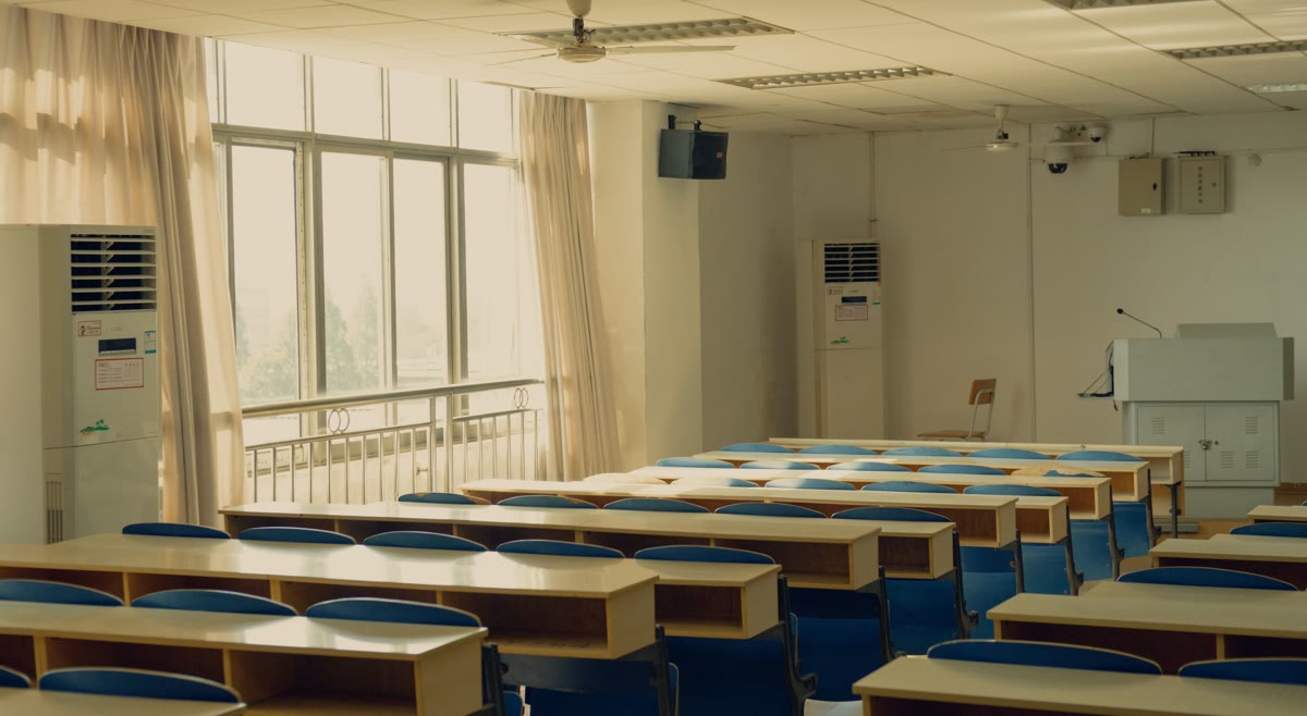 Sala de aula com carteiras enfileiradas e um ar-condicionado de piso ao fundo