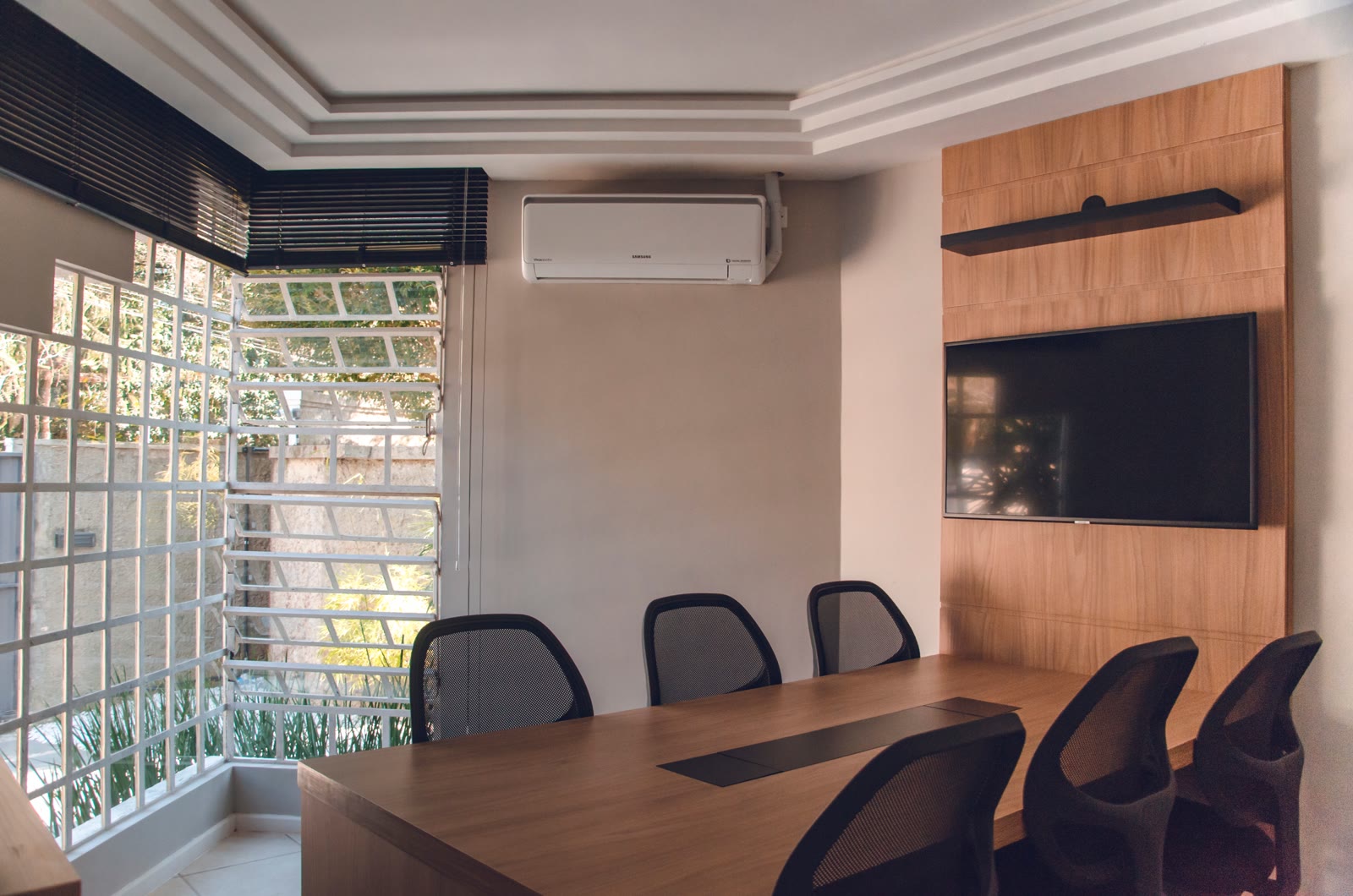 Sala de reunião com mesa de madeira, cadeiras e um ar-condicionado split na parede, perto do teto