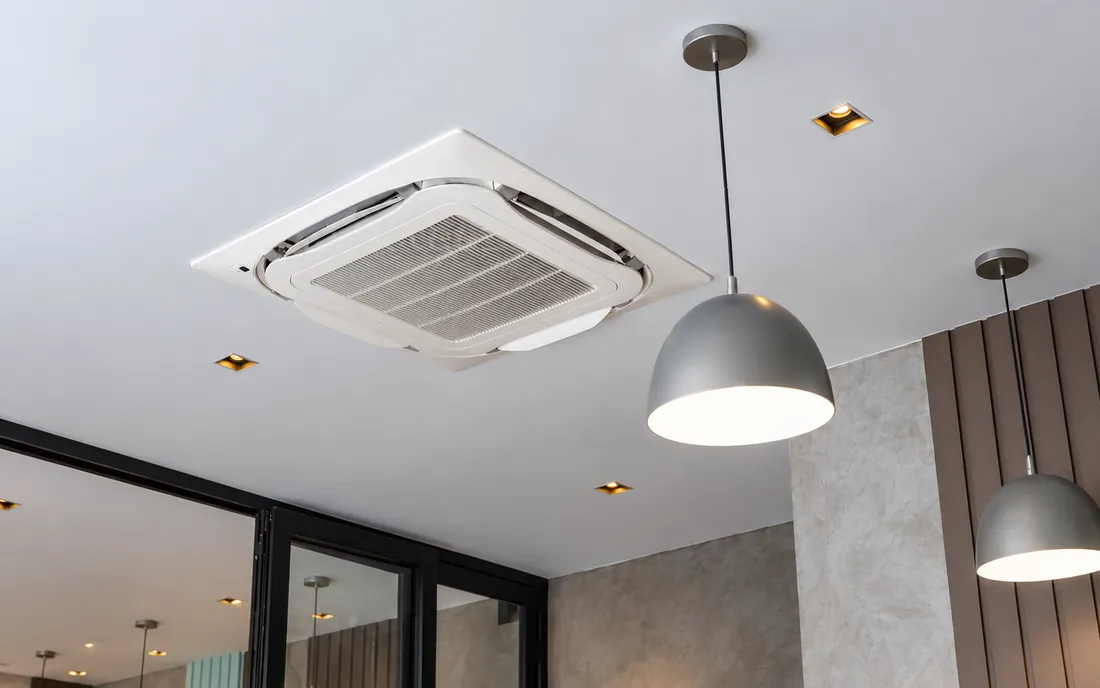 Ar-condicionado cassete embutido no teto, ao lado de luminárias pendentes