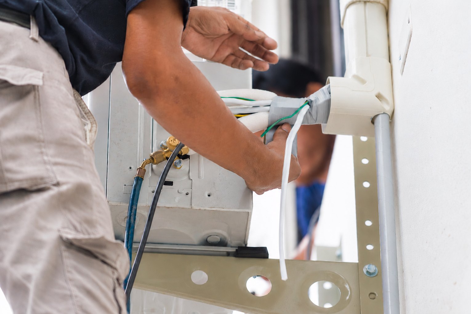 Técnico ligando a tubulação e os cabos na unidade externa do ar-condicionado, presa no suporte da parede